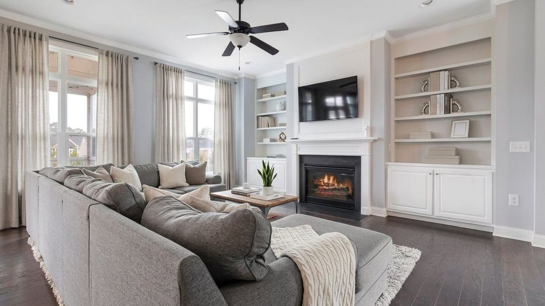 The same living room staged: neutral linen curtains and pillows, same gray sectional, shelves styled and simplified