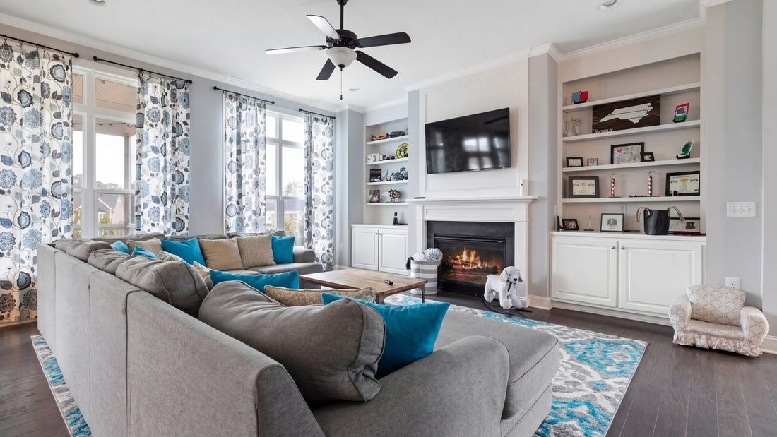 Occupied living room before staging: floral curtains, bright teal pillows, busy rug and crowded shelves